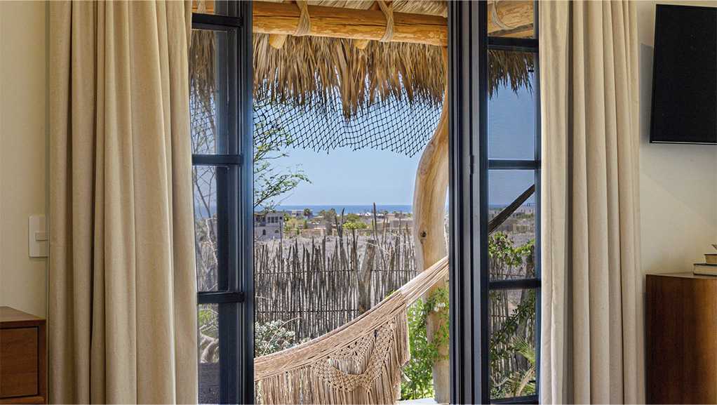 Framed ocean view from a Todos Santos residence, through linen curtains and a palapa terrace with a hammock.